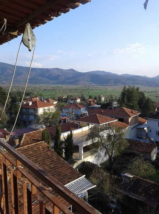 Red-tiled rooftops of Güney seen from a wooden balcony, with green fields and mountains behind